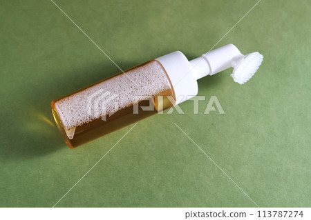 Beige facial foam with a dispenser and brush in a green background. Beige facial foam with a dispenser and brush in a green background. 113787274