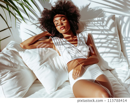 Woman lounging in sunlight, shadows of leaves casting over her 113788414