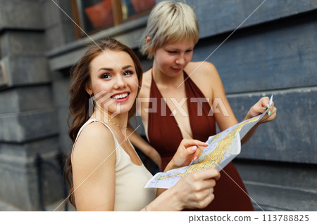 Happy young two women tourist travelers with paper map is exploring new city 113788825