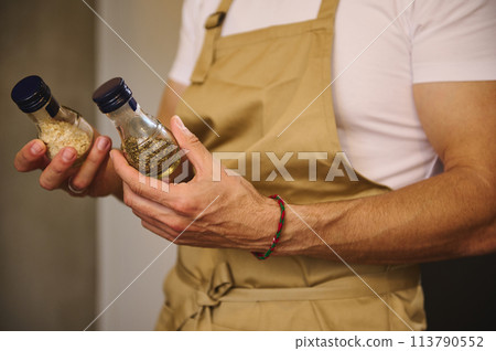 Close-up chef hands holding two glass bottles with condiments for seasoning dish while cooking dinner 113790552