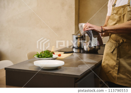 Close-up male chef wiping wet hands with kitchen towel while cooking dinner at home kitchen. People and domestic life. Culinary concept Close-up male chef wiping wet hands with kitchen towel while cooking dinner at home kitchen. People and domestic life. Culinary concept 113790553