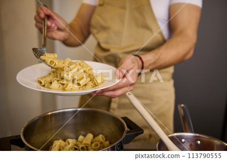 Close-up male chef pouring freshly cooked Italian past into a plate, ready to serve it to the customers Close-up male chef pouring freshly cooked Italian past into a plate, ready to serve it to the customers 113790555
