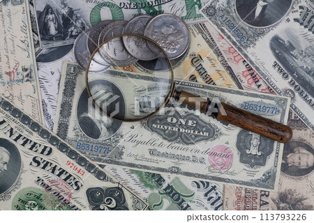 Old US banknotes and silver certificates with silver dollar coins and magnifying glass 113793226