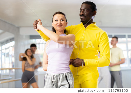 Middle-aged man and woman practicing waltz dance in pair in training hall 113795100