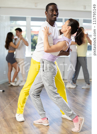 Happy African american man in pair with young woman dancing and training latin dance movements in ballroom together Happy African american man in pair with young woman dancing and training latin dance movements in ballroom together 113795149