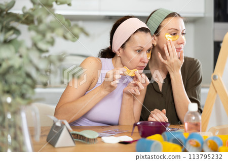 Two besties applying golden under-eye patches in home setting Two besties applying golden under-eye patches in home setting 113795232