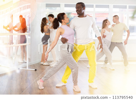 Happy African american man in pair with young woman dancing and training latin dance movements in ballroom together Happy African american man in pair with young woman dancing and training latin dance movements in ballroom together 113795540