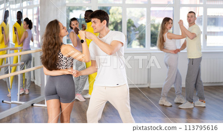 Happy young man and girl with group of international dancers training active swing in dance class Happy young man and girl with group of international dancers training active swing in dance class 113795616