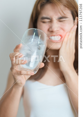 Teeth Sensitive to Cold concept. woman hold Ice Water glass and having toothache and pain after eat. Tooth Decay or Gum Disease, Grinding Teeth and Stress, Exposed Nerve Roots, Crack and Receding Gums Teeth Sensitive to Cold concept. woman hold Ice Water glass and having toothache and pain after eat. Tooth Decay or Gum Disease, Grinding Teeth and Stress, Exposed Nerve Roots, Crack and Receding Gums 113797208