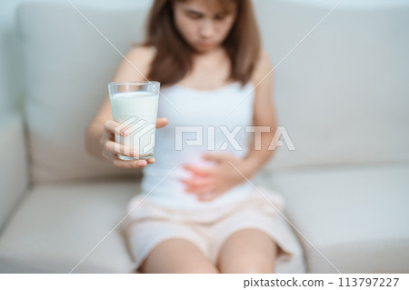 Lactose intolerance and Milk allergy concept. woman hold Milk glass and having abdominal cramps and pain when drink Cow Milk. Symptom stomach ache, Dairy intolerant, Nausea, Bloating, Gas and Diarrhea 113797227