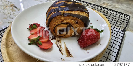 Fresh homemade striped chocolate croissant with chocolate filling on a round white plate, served with fresh strawberry Fresh homemade striped chocolate croissant with chocolate filling on a round white plate, served with fresh strawberry 113797377