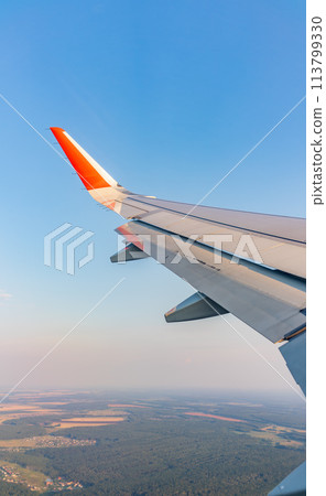 View of airplane wing, blue skies and green land during landing. Airplane window view. 113799330