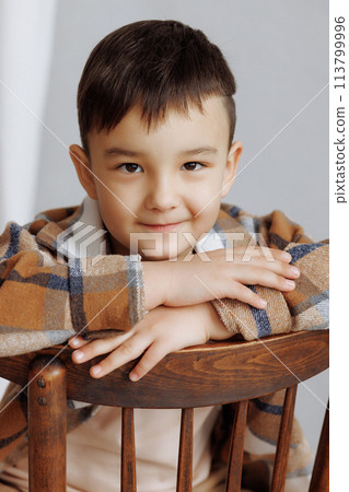 A young boy is sitting on a wooden chair with a stuffed animal in his lap A young boy is sitting on a wooden chair with a stuffed animal in his lap 113799996