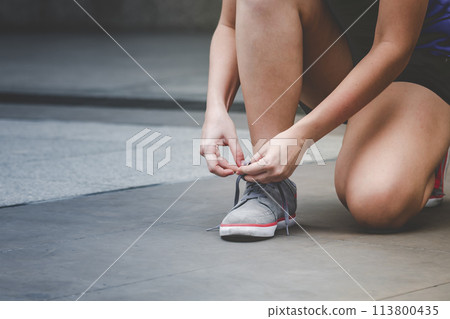Sport sneakers footwear young woman knelt down do up shoelaces. Ready running shoes in sport exercise jogging person. Close up hands tie up runner shoelaces in fitness gym healthy person lifestyle. Sport sneakers footwear young woman knelt down do up shoelaces. Ready running shoes in sport exercise jogging person. Close up hands tie up runner shoelaces in fitness gym healthy person lifestyle. 113800435
