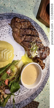 Beef New York strip loin steak or sirloin steak served with potatoes, and mushroom sauce and salad on plate Beef New York strip loin steak or sirloin steak served with potatoes, and mushroom sauce and salad on plate 113800608