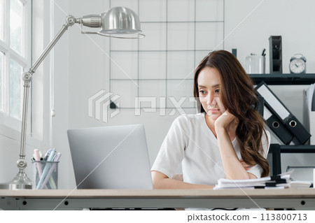 A woman is sitting at a desk with a laptop and a clock on the wall A woman is sitting at a desk with a laptop and a clock on the wall 113800713