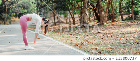 Woman in pink leggings touches her toes while stretching on a park path, surrounded by trees and fallen leaves. Woman in pink leggings touches her toes while stretching on a park path, surrounded by trees and fallen leaves. 113800737