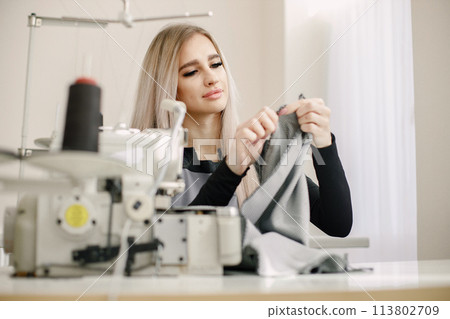 Young seamstress sitting on the sewing machine in her workshop 113802709