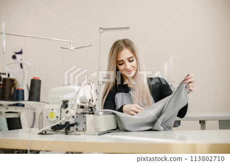 Young seamstress sitting on the sewing machine in her workshop 113802710