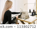 Young seamstress sitting on the sewing machine in her workshop 113802712