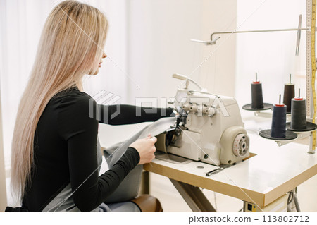 Young seamstress sitting on the sewing machine in her workshop 113802712