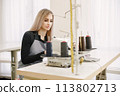 Young seamstress sitting on the sewing machine in her workshop 113802713