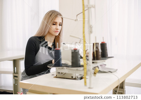Young seamstress sitting on the sewing machine in her workshop 113802713