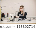Young seamstress sitting on the sewing machine in her workshop 113802714