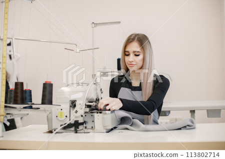 Young seamstress sitting on the sewing machine in her workshop Young seamstress sitting on the sewing machine in her workshop 113802714