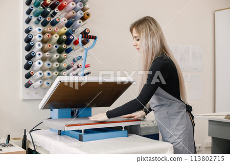 Young dressmaker standing in workshop near the bright wall with threads Young dressmaker standing in workshop near the bright wall with threads 113802715