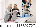 Two dressmakers standing in workshop near the bright wall with threads 113802727