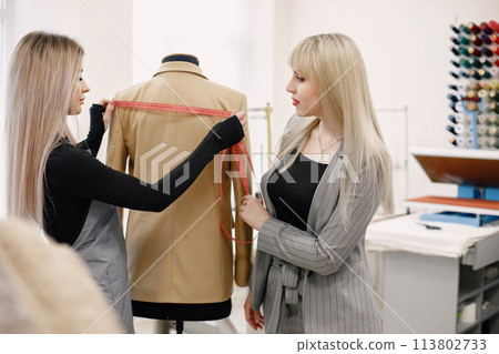 Female dressmaker measuring jacket on dummy to make recesses 113802733