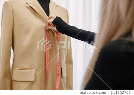 Female dressmaker measuring length on dummy to make recesses 113802735