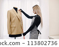 Female dressmaker measuring sleeve length on dummy to make recesses 113802736