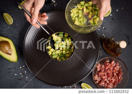 Tuna and avocado tartare recipe - woman fills cooking form with sliced chopped avocado 113802832