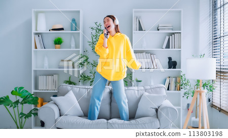 On the sofa in her living room, a young Asian woman dances On the sofa in her living room, a young Asian woman dances 113803198