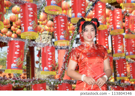 Portrait pretty Asian female in red traditional Chinese costume standing and posing in front of the lanterns in the shrine. Portrait pretty Asian female in red traditional Chinese costume standing and posing in front of the lanterns in the shrine. 113804346