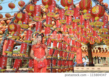 Portrait pretty Asian female in red traditional Chinese costume standing and posing in front of the lanterns in the shrine. 113804347