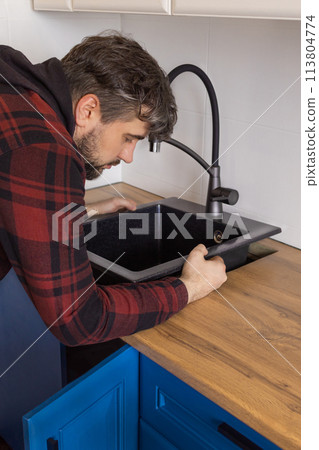 Man installing black stone sink into wooden countertop in kitchen. Vertical Man installing black stone sink into wooden countertop in kitchen. Vertical 113804774