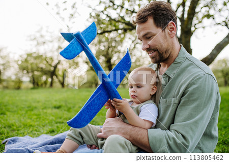 Father and toddler playing with foam glider plane. Single dad having fun with baby during warm spring day. Father's day concept. 113805462