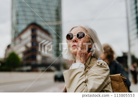 Portrait of stylish mature woman with gray hair on city street. Older woman in sunglasses waiting for public transport. Portrait of stylish mature woman with gray hair on city street. Older woman in sunglasses waiting for public transport. 113805553