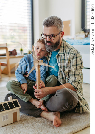 Father explaining renewable energy, teaching about sustainable lifestyle his young son. Playing with house with solar panels, wind turibine at home. Father explaining renewable energy, teaching about sustainable lifestyle his young son. Playing with house with solar panels, wind turibine at home. 113805696
