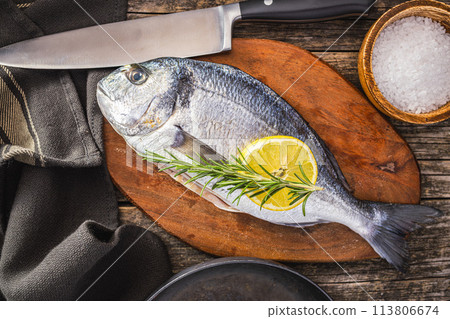 Fresh sea bream fish on cutting board on wooden table. Top view. 113806674