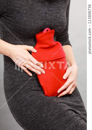 Girl having stomach ache, holding hot water bottle 113806736