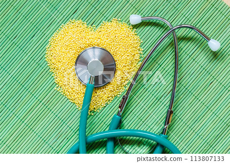 Millet groats heart shaped on green mat surface. 113807133