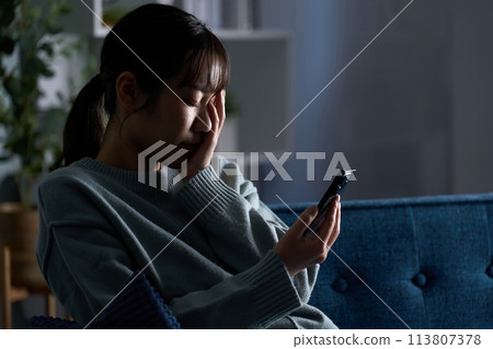 A depressed woman looking at a smartphone 113807378