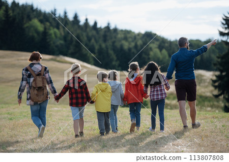 Young students walking across meadow during biology field teaching class, holding hands. Dedicated teachers during outdoor active education teaching about ecosystem, ecology. 113807808