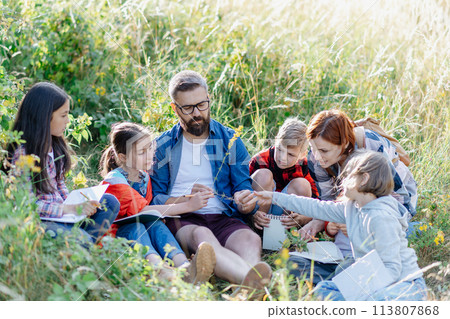 Young students learning about nature, forest ecosystem during biology field teaching class, observing wild plants, taking notes. Dedicated teachers during outdoor active education. Young students learning about nature, forest ecosystem during biology field teaching class, observing wild plants, taking notes. Dedicated teachers during outdoor active education. 113807868
