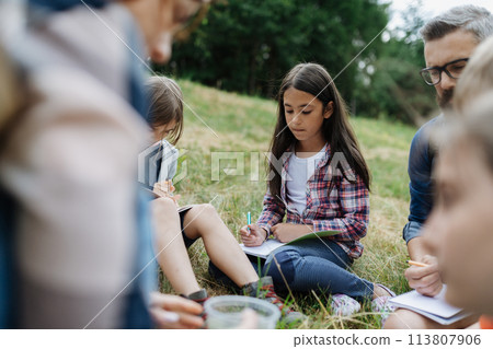 Young students learning about nature, forest ecosystem during biology field teaching class, writing notes. Male teacher during outdoor active education. 113807906