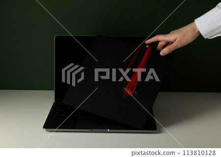 A graduate's hat on a laptop, on a green background. A graduate's hat on a laptop, on a green background. 113810128